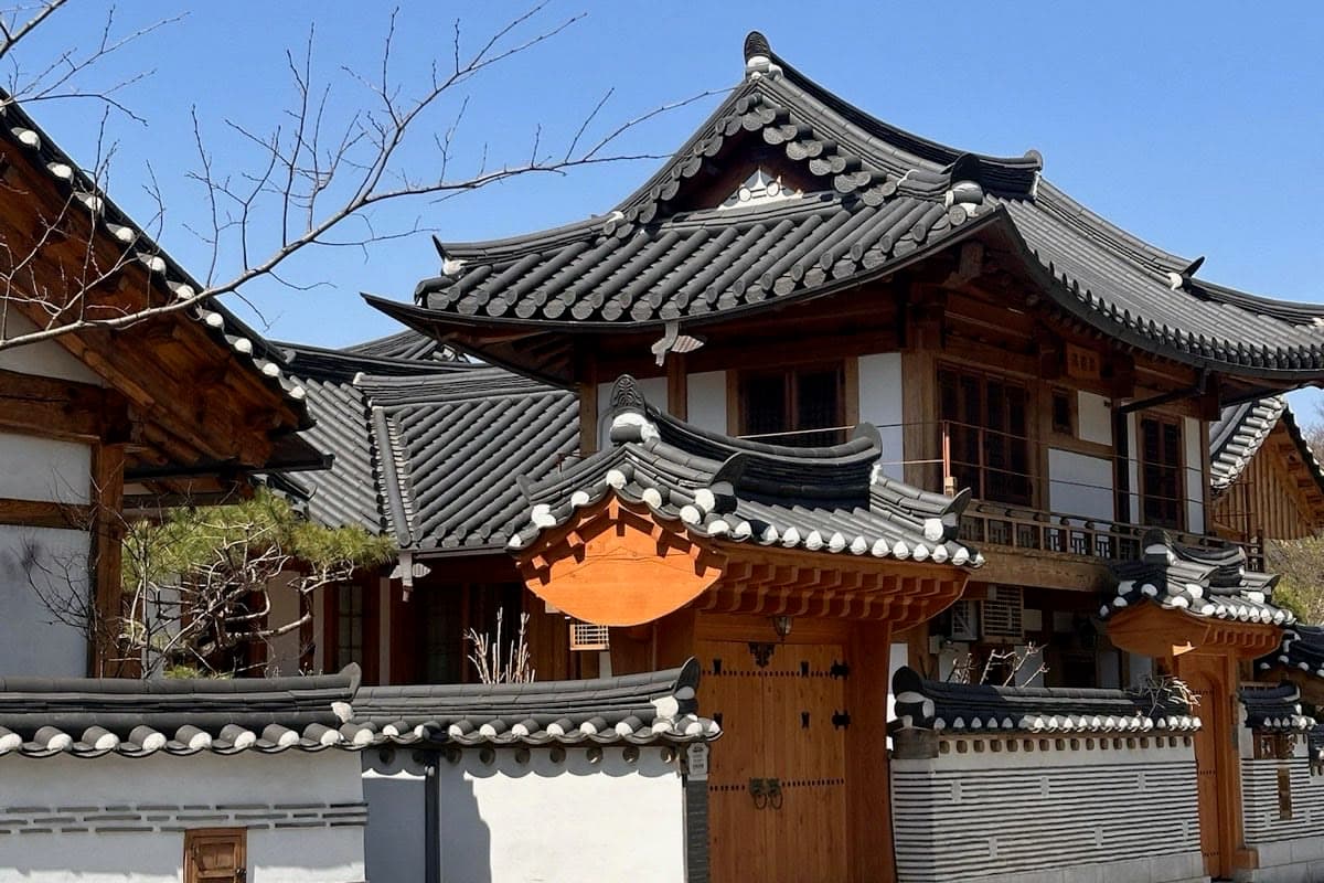 Maisons traditionnelles coréennes aux toits de tuiles derrière une palissade en bois, sous un ciel bleu