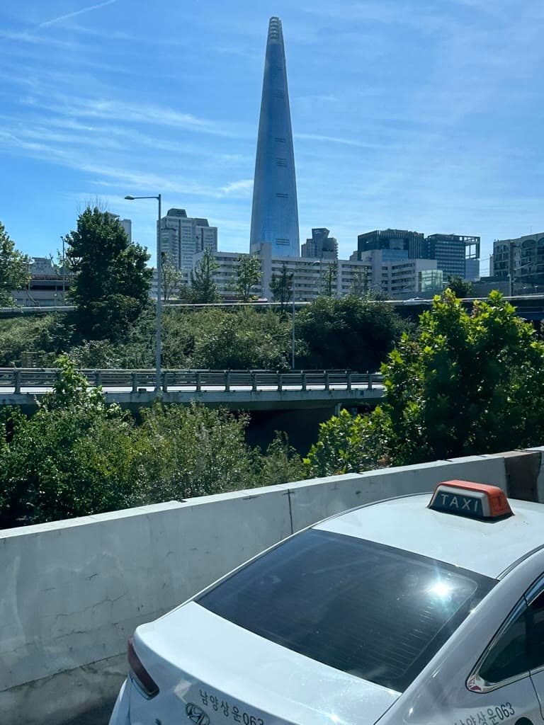 Taxi blanc de Séoul avec son enseigne TAXI orange, devant la tour Lotte World et des arbres